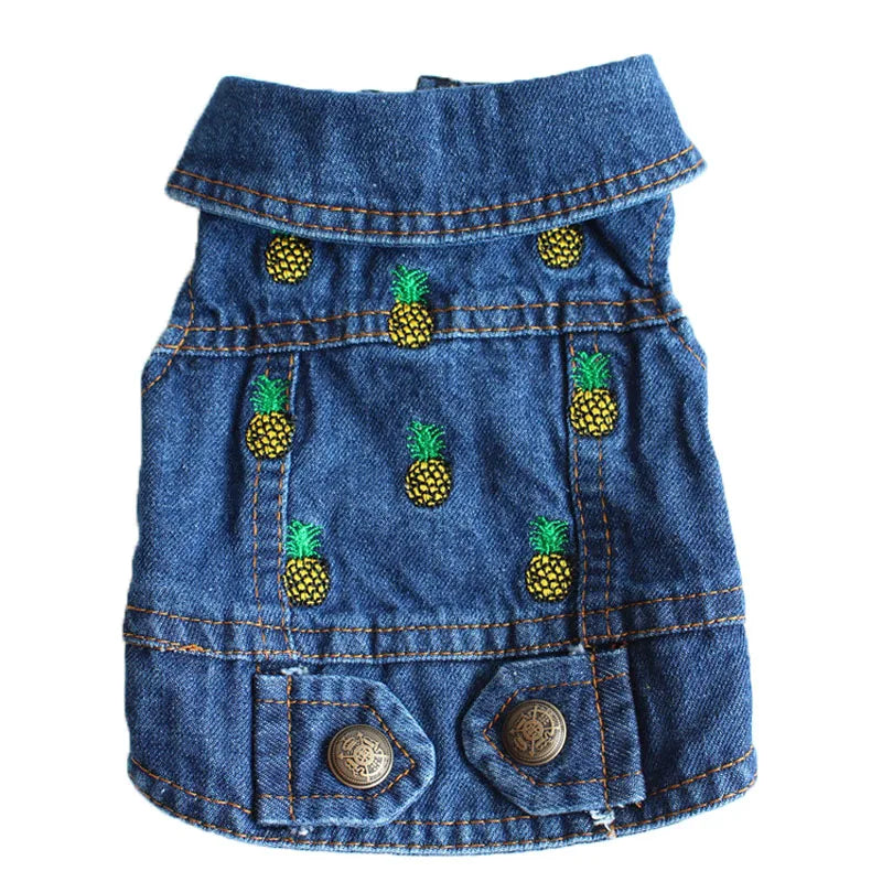 A blue denim pet jacket decorated with embroidered pineapple motifs, featuring a collar, front pockets, and metal buttons, shown against a plain white background.