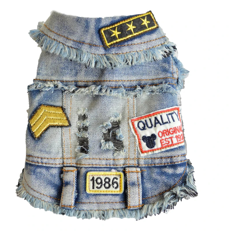 A miniature denim vest for pets, styled like a military uniform jacket with frayed edges, faux distressing, and various embroidered patches including a three-star patch, chevron, and a 'QUALITY' patch.
