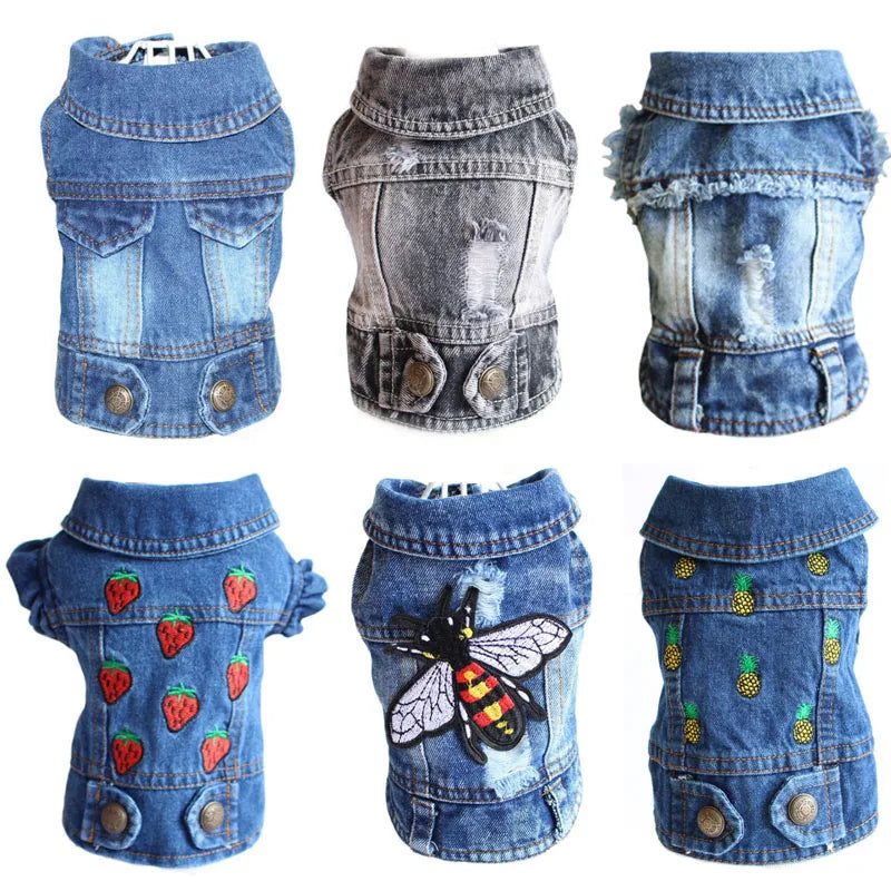 Six small denim pet jackets arranged in a 2x3 grid on a white background, each with a different design: plain blue, faded gray, distressed blue, blue with strawberry patches, blue with a bee patch, and blue with pineapple patches.