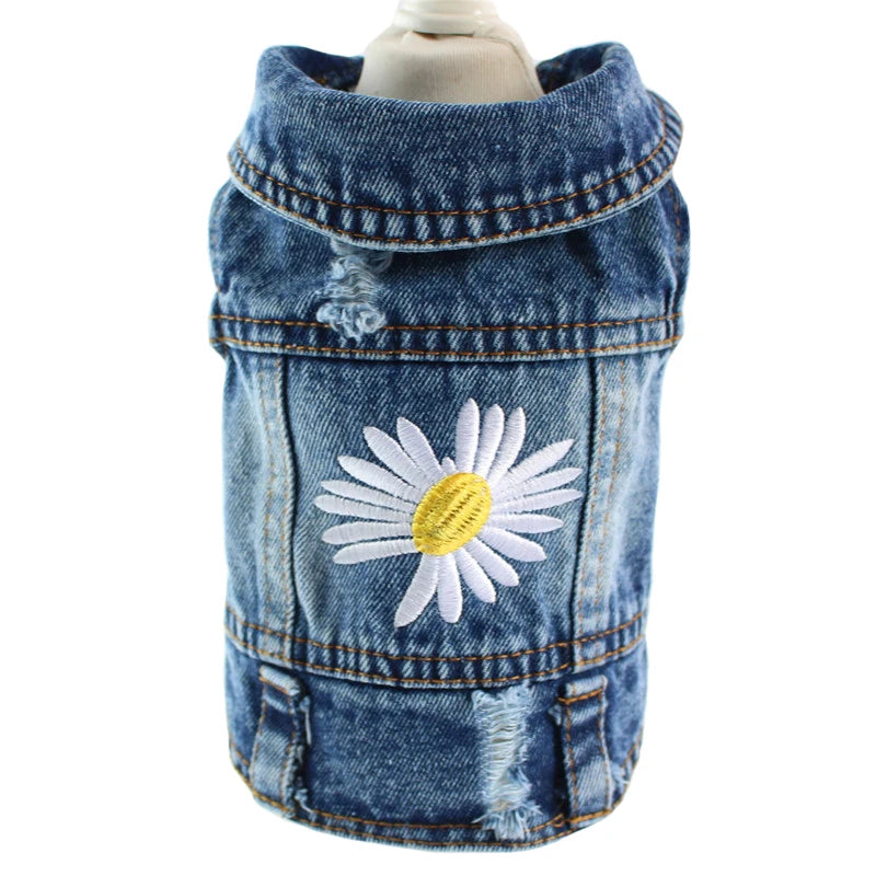 A blue denim pet jacket with a white and yellow embroidered daisy on the front, displayed on a mannequin torso against a white background.