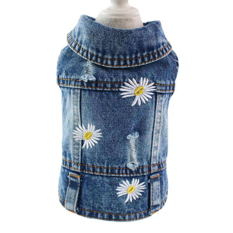 A blue denim pet vest with embroidered daisy flowers and distressed details, displayed on a mannequin torso against a white background.