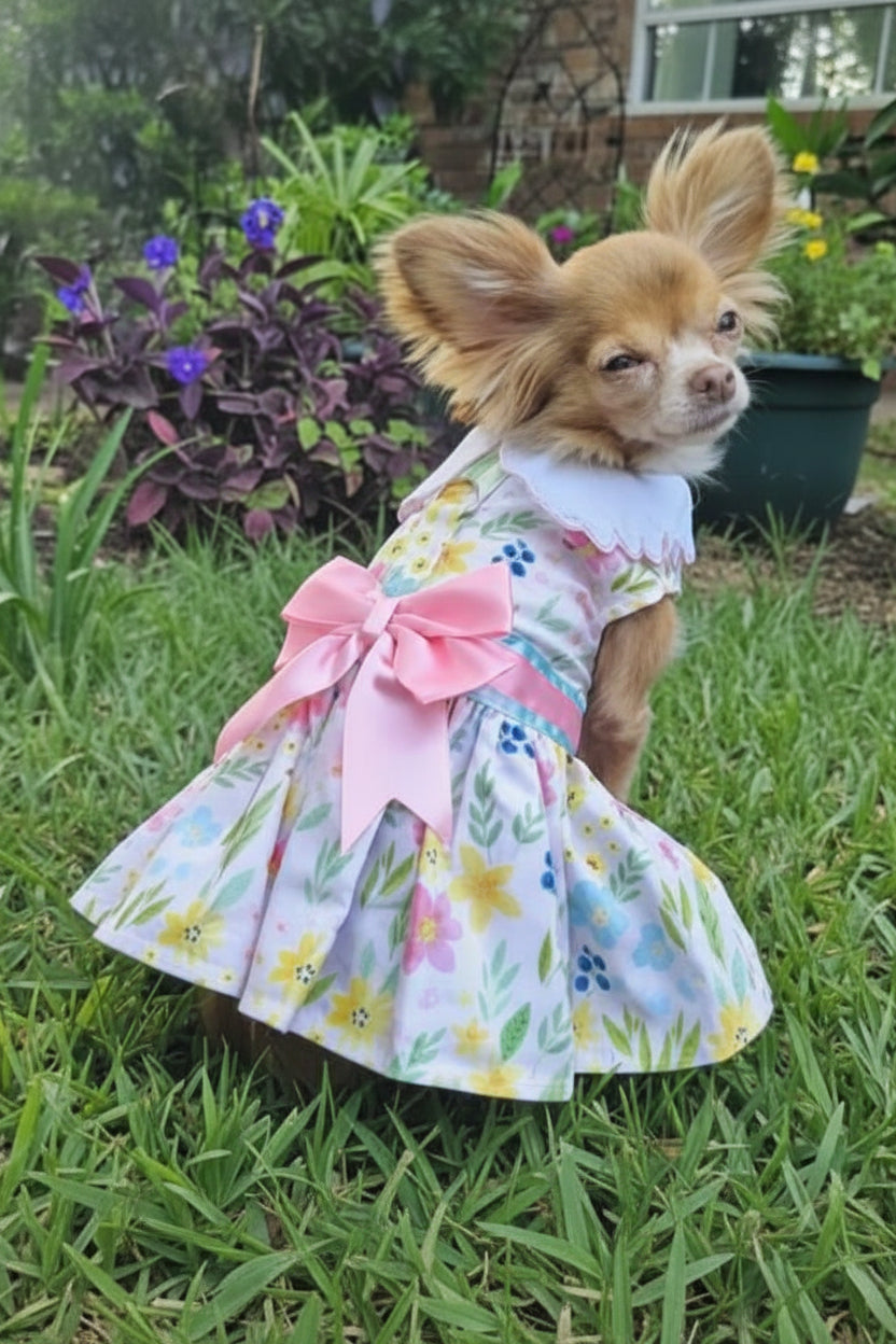Dog wearing a floral dress with a pink bow in a garden setting